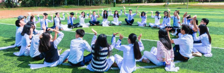 People Sitting on Green Lawn Grass While Doing Hands Up at Daytime