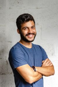 Portrait Photo of Smiling Man with His Arms Crossed Standing In Front of a Wall